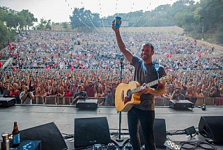 jack johnson holding up reusable cup on stage with crowd cheering in the background