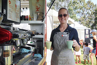 young woman working at coffee van holding two reusable mugs with coffee